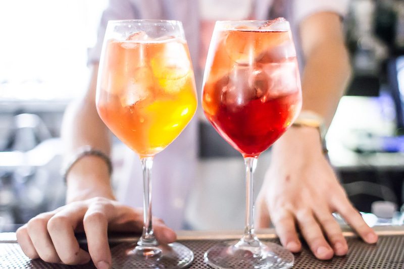 винные бокалы с двумя коктейлями - напиток жёлтого и рубинового красного цвета на барной стойке подача со льдом от бармена