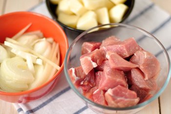 Нарезанные крупными кусочками мясо свинины лук и картофель для приготовления айнтопфа