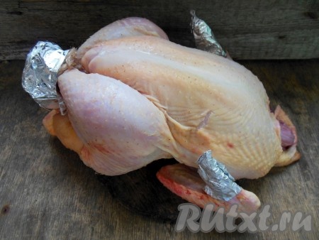 Тушку курицы необходимо хорошо промыть внутри и снаружи. Обсушить с помощью бумажного полотенца. Ножки курицы нужно связать между собой. Ножки и крылышки оберните фольгой (как на фото), чтобы в процессе запекания они не подгорали.
