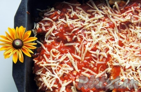 Добавить томатный соус, распределив его ровным слоем по мясу. Обильно посыпать куриные отбивные тёртым сыром и поставить запекаться на 20 минут.