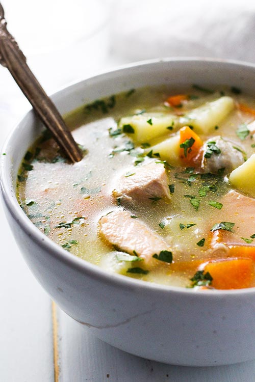 A bowl of Ukha, Russian fish soup with a rustic spoon. Fish is gently cooked with potatoes and carrots in a rich broth seasoned with bay and black pepper. 