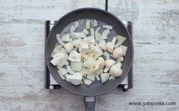 К луку добавьте крупно нарезанные грибы и измельченный чеснок. Обжаривайте несколько минут до золотистости.