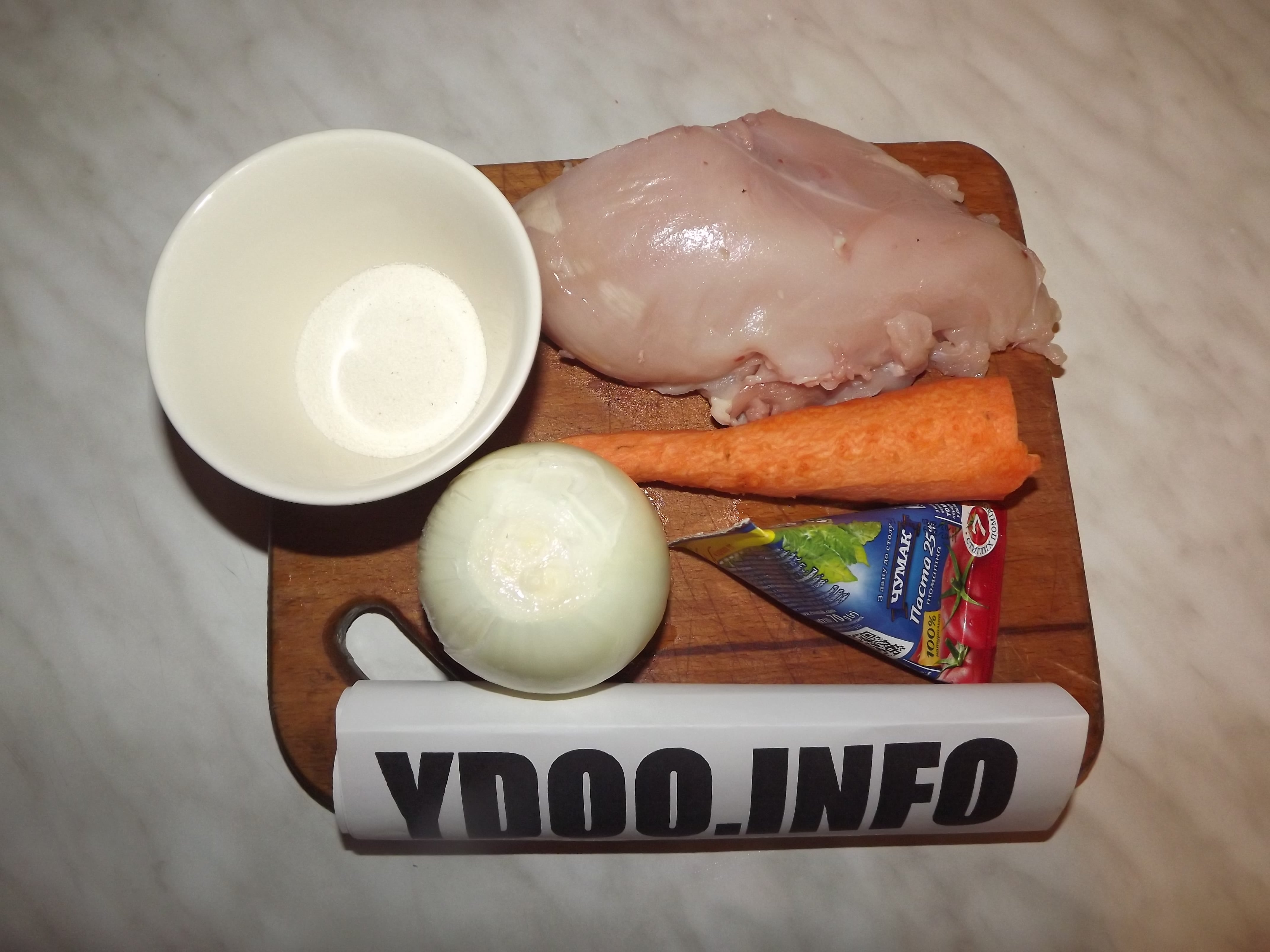 куриное филе, очищенные морковь и луковица, мука в чашке, треугольнмк томатной пасты на деревянной разделочной доске на столе