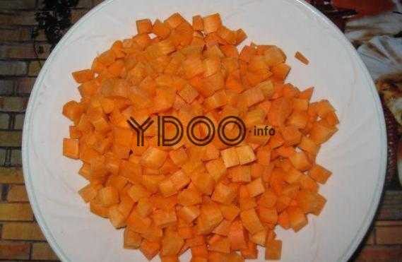 морковь, нарезанная кубиками, в белой тарелке на столе