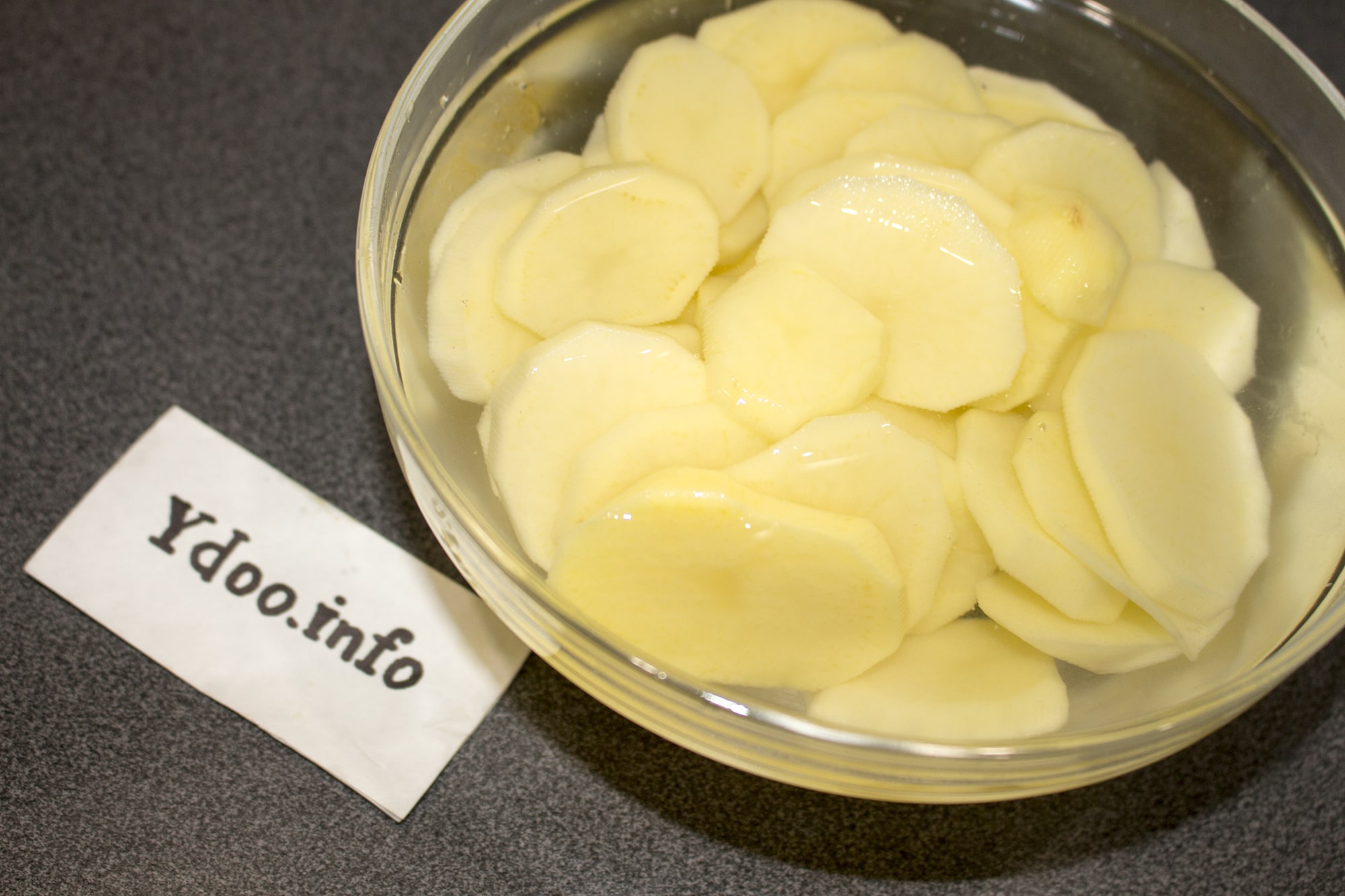сырой картофель, нарезанный кружочками, в стеклянной мисочке с водой
