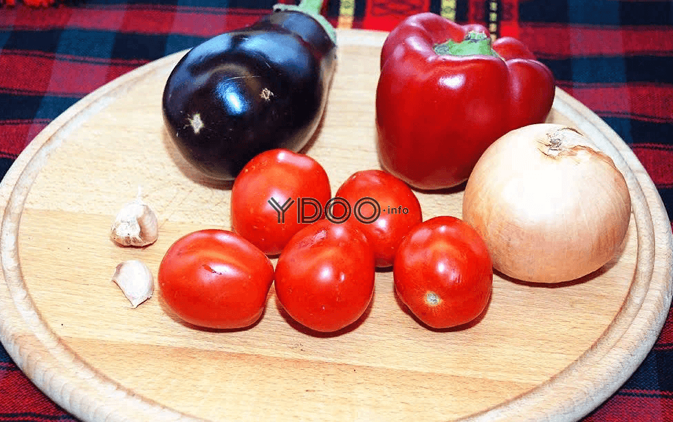 баклажан, красный болгарский перец, репчатая луковица, пять небольших помидоров, два зубчика чеснока на круглой деревянной разделочной доске