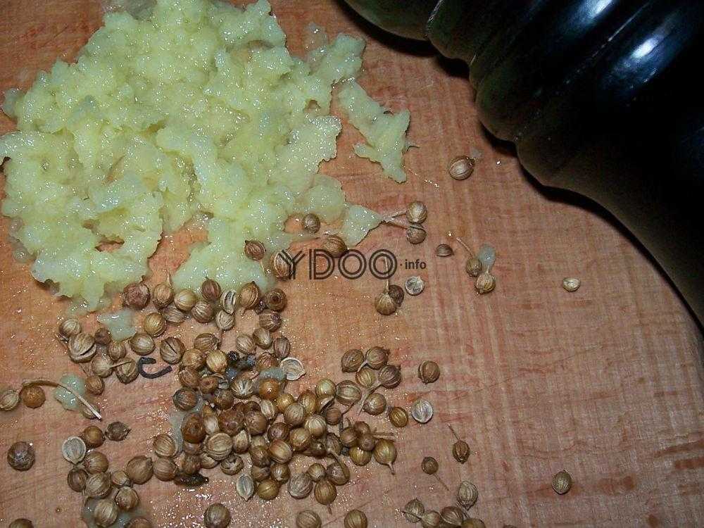 измельченный чеснок и зерна кориандра на деревянной разделочной доске