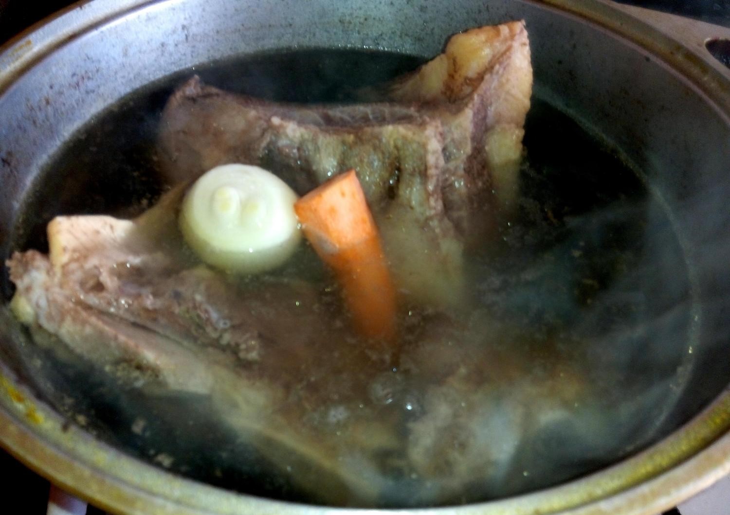 кусок говядины с целым луком и морковью, покрытый водой, в кастрюле