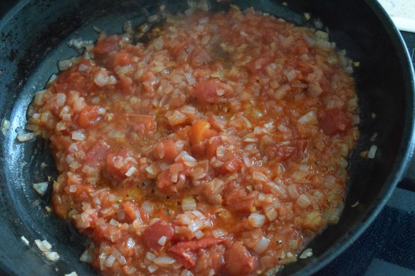 жареные кусочки репчатого лука и помидоров в сковороде