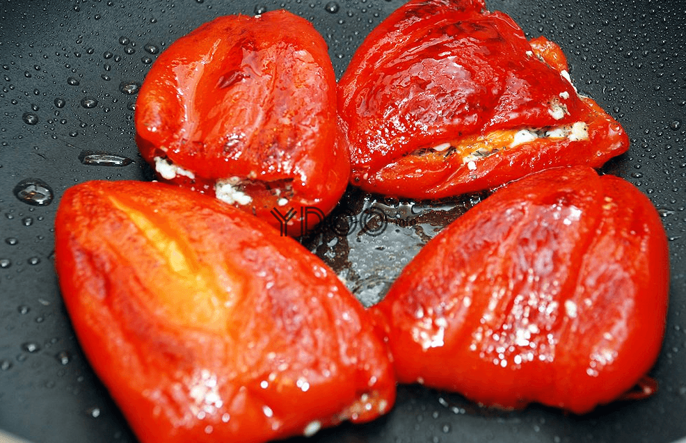 четыре красных болгарских ерца с начинкой жарятся на сковороде с растительным маслом