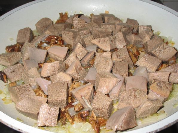кусочки вареного говяжьего языка, перемешанные с жареными репчатым луком и грибами в сковороде