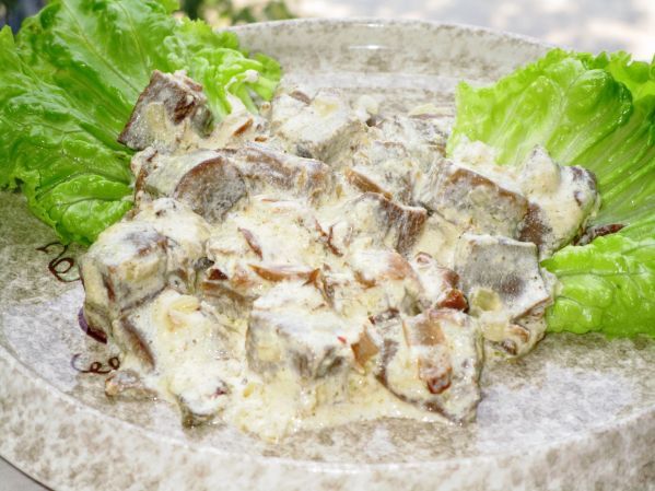 тушеные кусочки грибов и говяжьего языка, политые сметанным соусом, на тарелке с салатными листьями