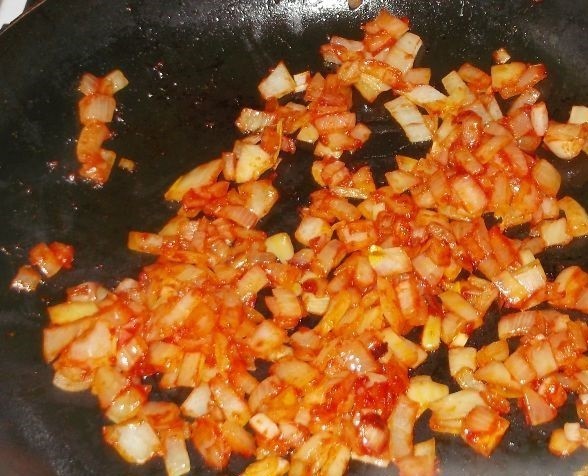 жареный репчатый лук, перемешанный с томатной пастой в сковороде