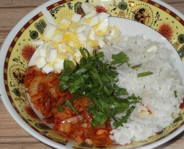 вареный рис, нарезанные яйца, жареный лук и зелень на тарелке на столе