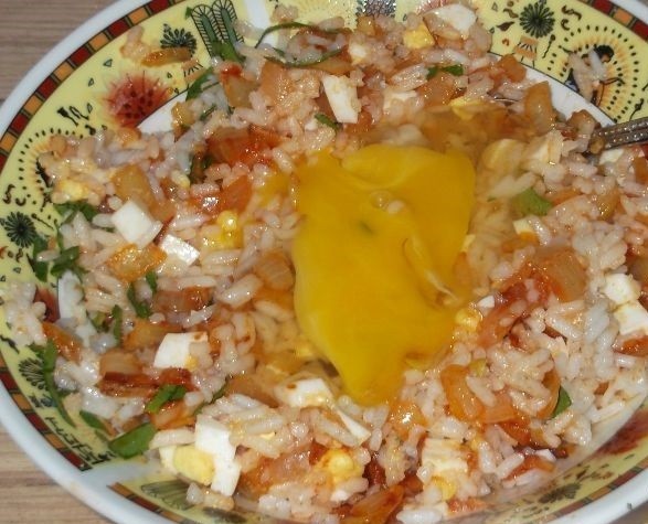 вареный рис, перемешанный с зеленью, яйцами и луком, с двумя сырыми куриными яйцами на тарелке на столе