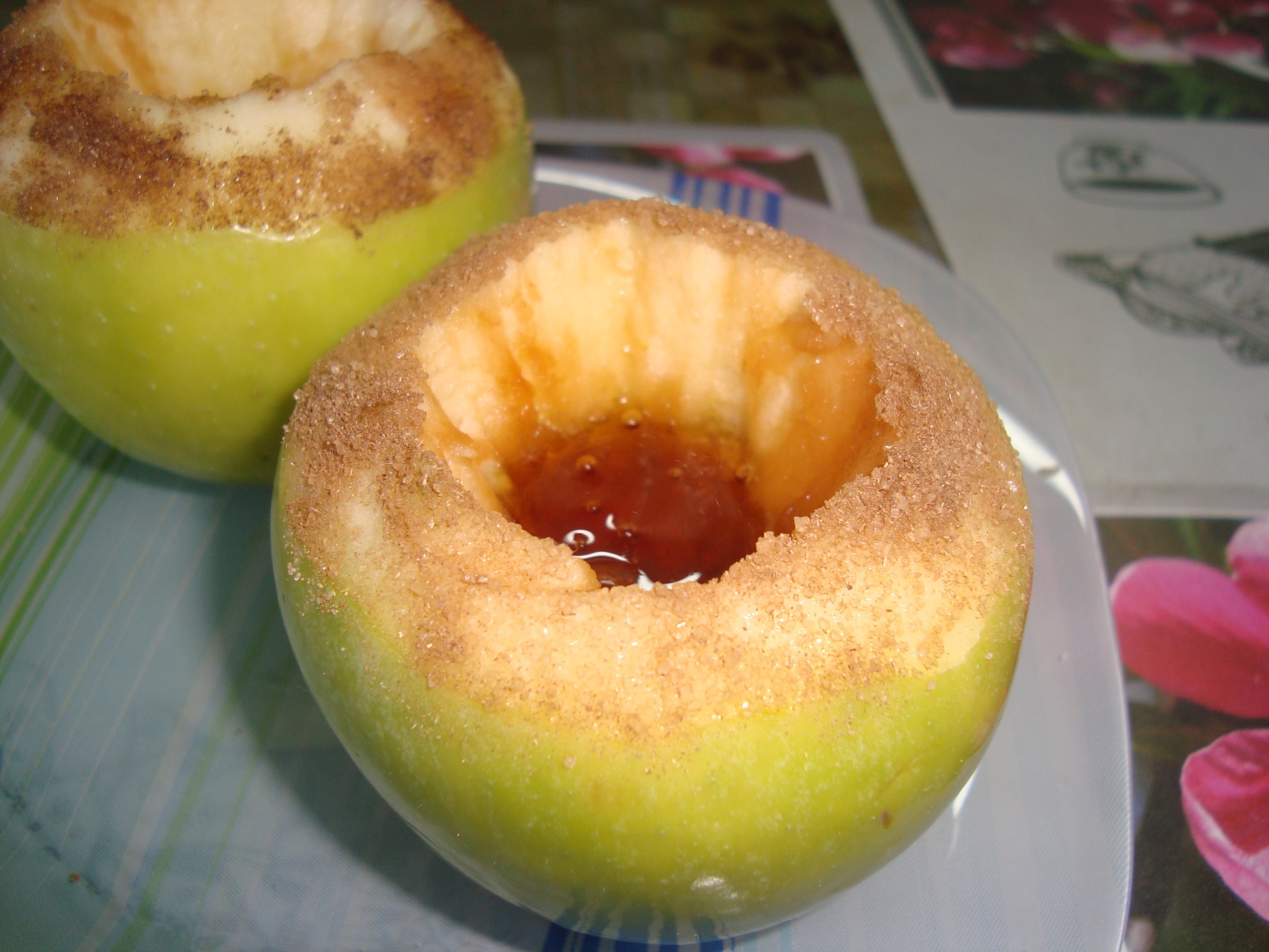 зеленое яблоко с медом внутри, присыпанное по краям сахаром, на тарелке