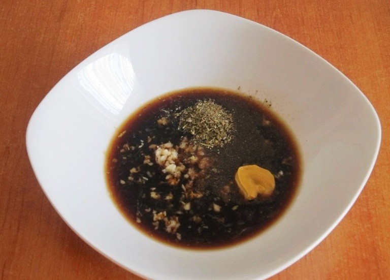 соевый соус с горчицей, измельченным чесноком и сухими травами в глубокой белой тарелке на столе