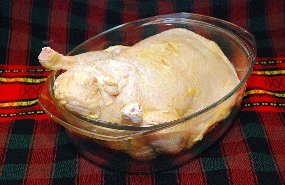 фаршированная сырая тушка утки, смазанная маслом, в стеклянном противне на столе, застеленном тканью