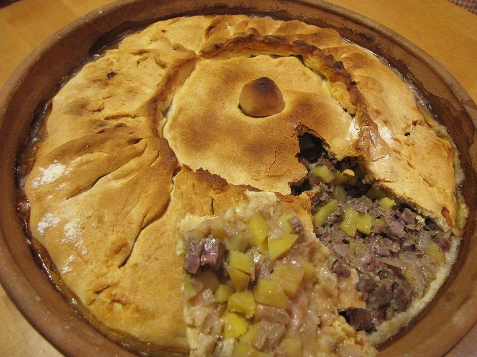 разрезанный зур бэлиш с кусочками говядины, репчатого лука и картофеля внутри, в форме для выпекания на столе