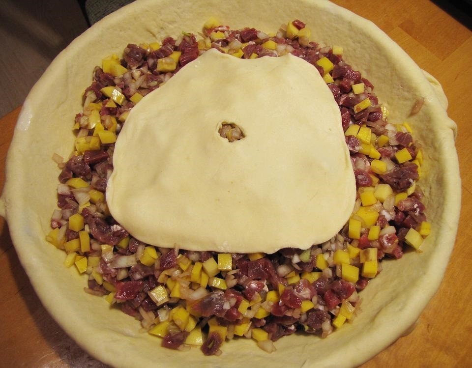 сырые кусочки говядины, перемешанные с репчатым луком и картофелем, выложенные в форму с тестом и накрытые пластом теста с отверстием в центре
