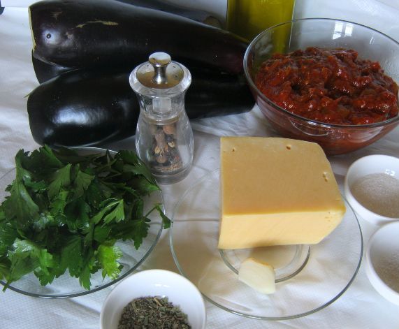 баклажаны, томатный соус, петрушка, кусок твердого сыра и зубчик чеснока на разных тарелках, сушеный орегано и соль в пиалах на столе