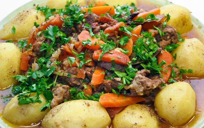 тушеные кусочки мяса с помидорами и картофелем, посыпанные рубленой зеленью, в тарелке