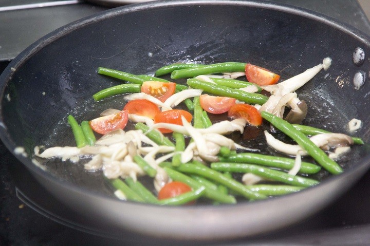 жареная стручковая фасоль с вешенками и кусочками черри в сковороде на плите